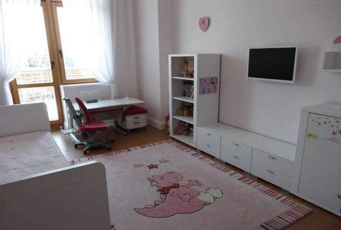 Mobili bianchi e tappeto rosa nella stanza dei bambini